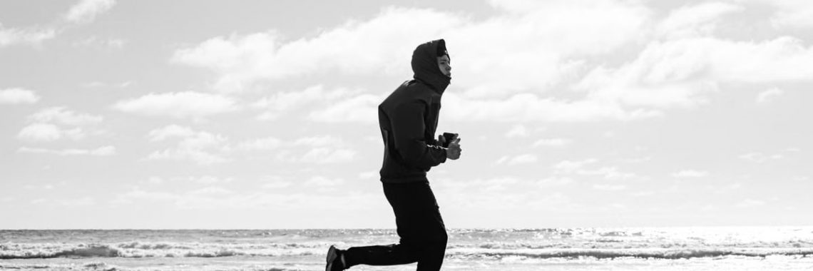 Silhouette of a jogger running along La Lucila del Mar beach, captured in monochrome.